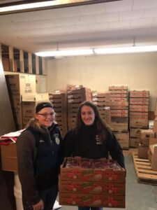Two people smiling in a storage room filled with boxes.