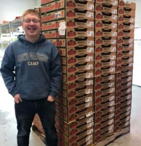 A smiling man stands beside a tall stack of pizza boxes.