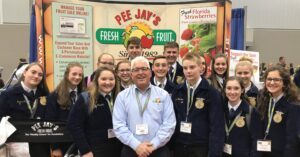 A group of young people and an adult stand together smiling indoors at a fruit stand.