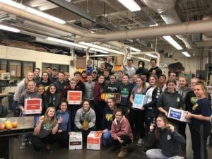 A large group of people posing indoors, holding colorful signs and smiling.