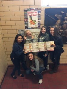 Five girls holding menus and posing in a cozy restaurant setting.